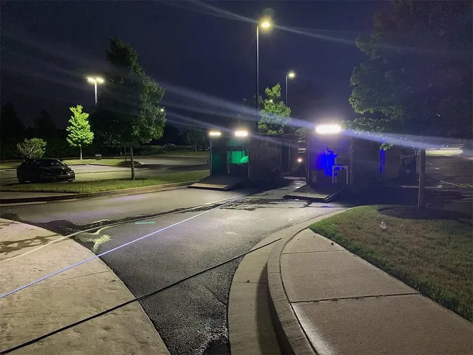 Night scene: parking lot with illuminated porta-potties, trees, streetlight, and a black car.