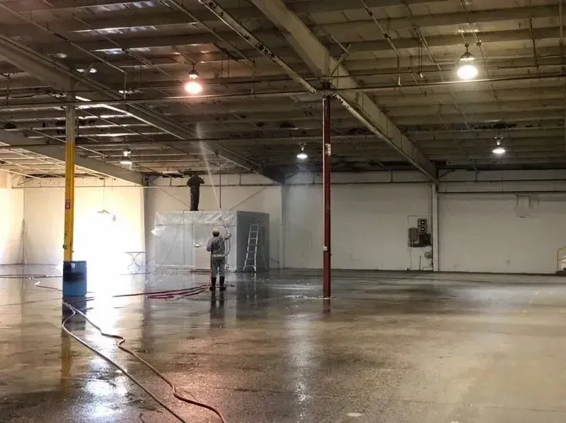 Person spraying water in a large, empty warehouse with a wet floor and exposed beams.