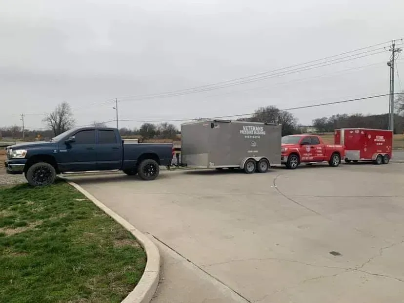 Dark blue pickup truck towing two trailers on a concrete lot on an overcast day.