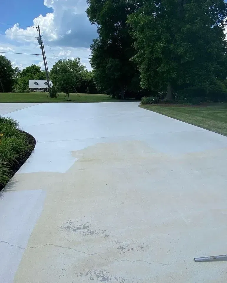 Light gray concrete driveway with faded stains, leading towards trees and a house.