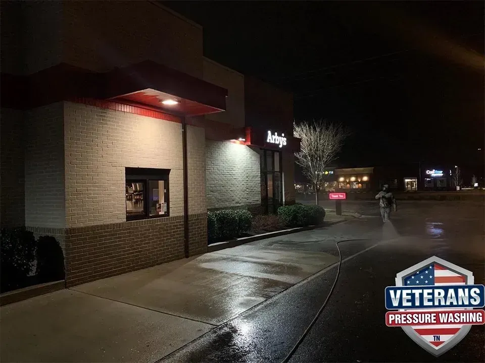 Exterior of an Arby's being pressure washed at night. A person sprays the wet concrete with water.