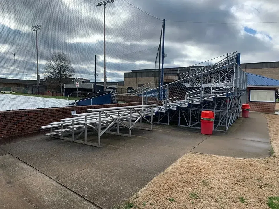 Empty bleachers at a baseball field on a cloudy day.