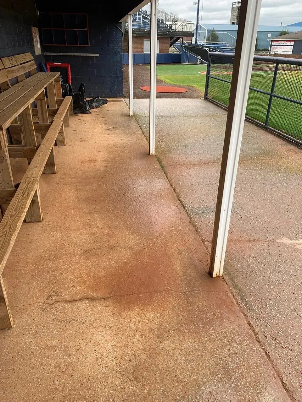 Baseball dugout interior; weathered concrete floor, wooden benches, supporting pillars, and field view.