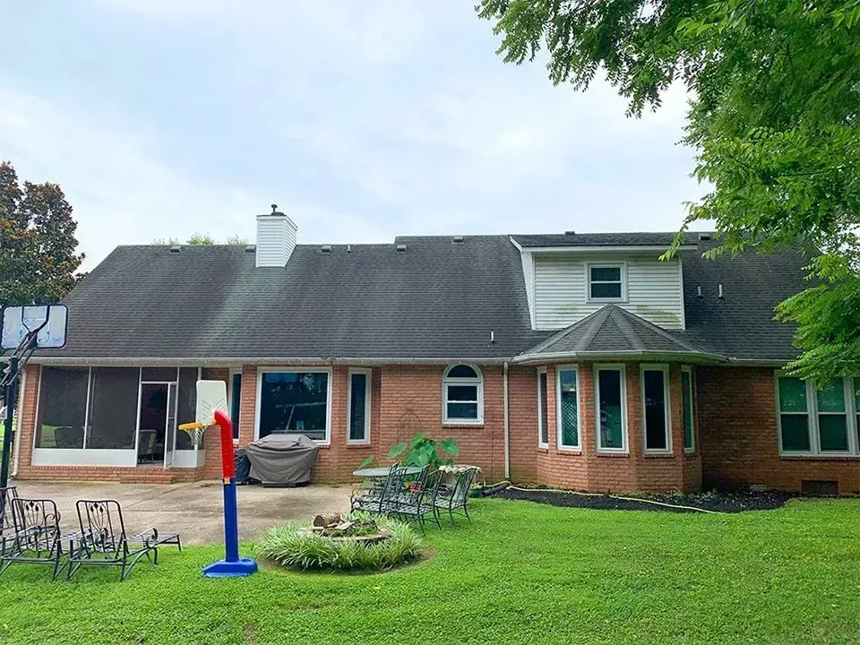 Brick house exterior with green lawn, basketball hoop, patio furniture, and overcast sky.
