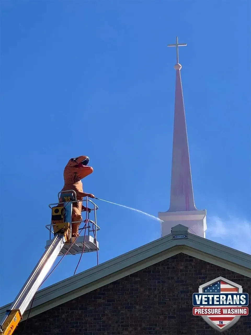 A dinosaur in a lift washing the pink spire of a church under a blue sky.