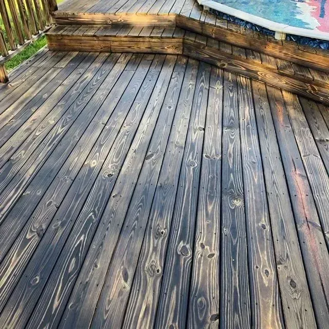 Wooden deck stained dark gray with visible wood grain, beside a partially visible pool.