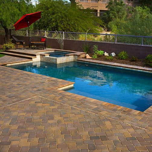 Pool with blue water, adjacent hot tub, brick patio, red umbrella, and seating area.