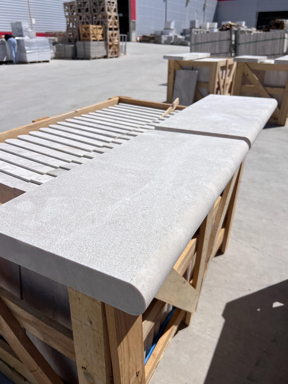 Stone coping tile with rounded edge, on wooden crate, warehouse setting.