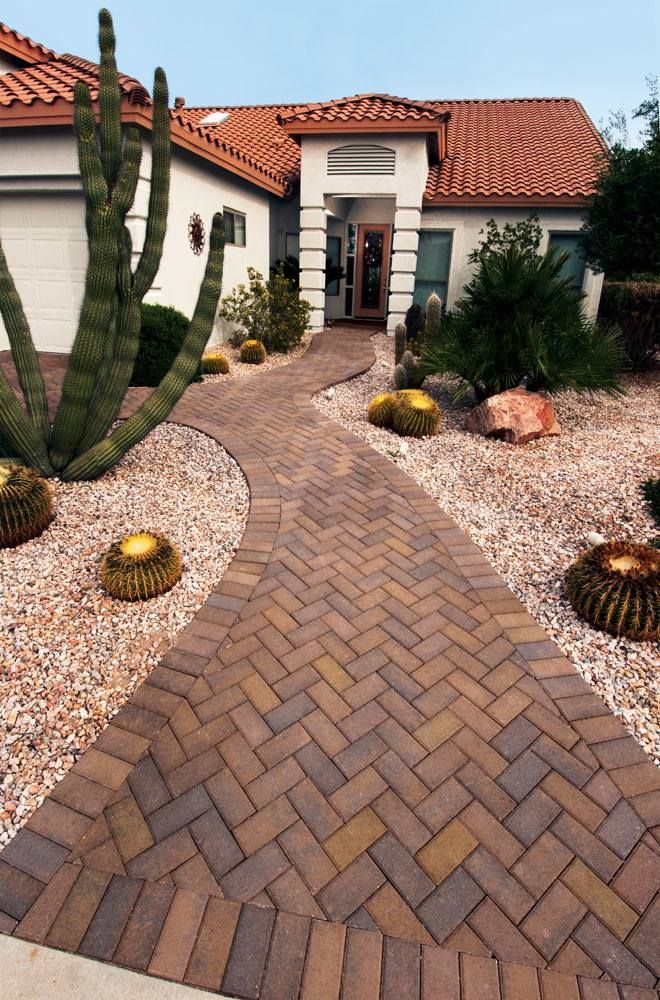 Brick walkway leading to a stucco house with desert landscaping.