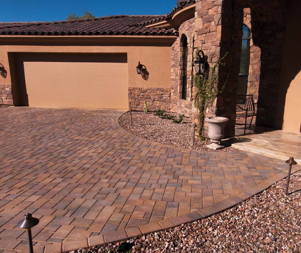 Brick paved driveway in front of a house with a garage, stone facade, and landscaping.