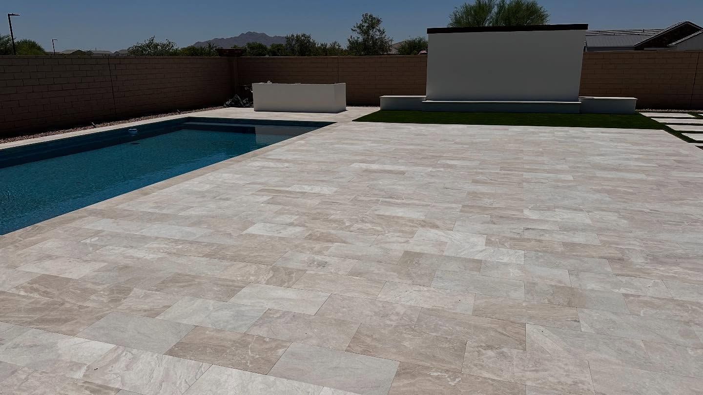 Backyard with pool, travertine patio, brick wall, and white wall with a small lawn.