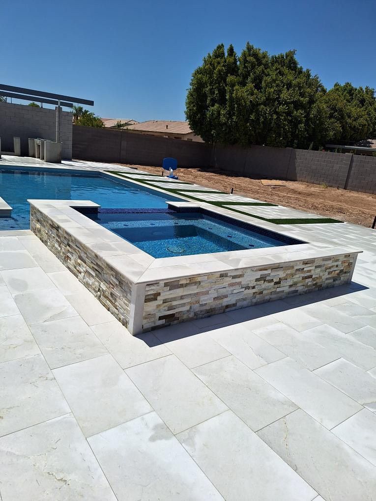 Pool area with a spa, blue water, stone facade, and patio under a sunny sky.