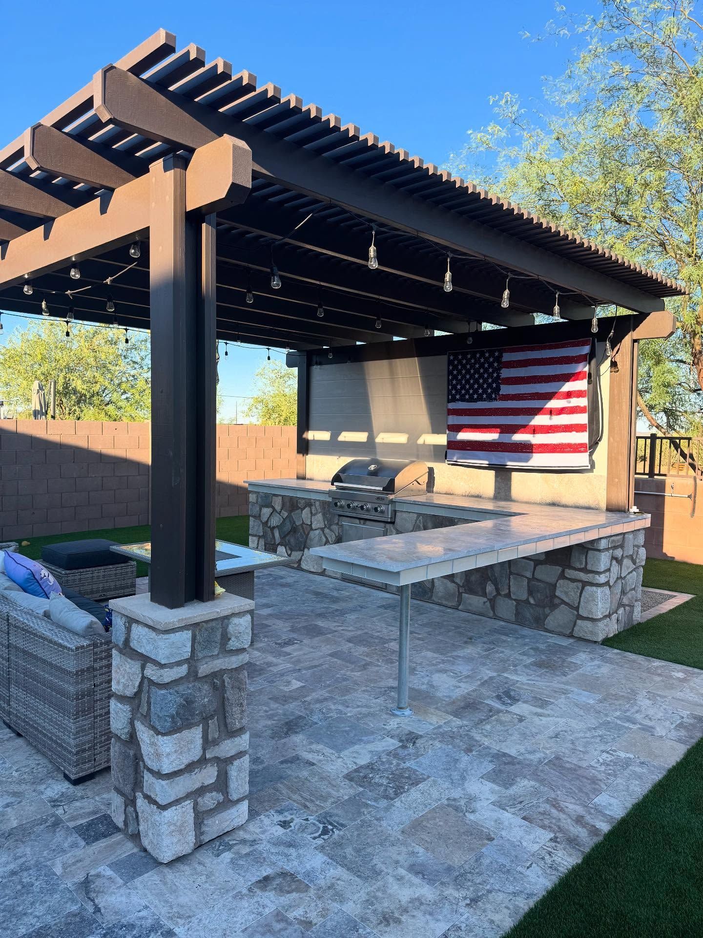 Outdoor kitchen with brown pergola, stone base, and American flag.