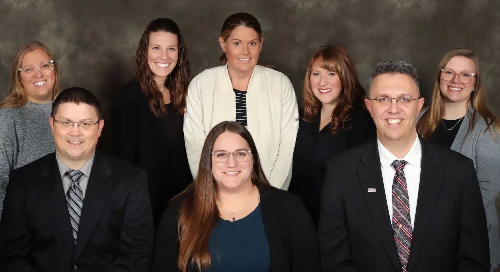 Group photo: Eight people, mostly women, in business attire pose in front of a dark background.
