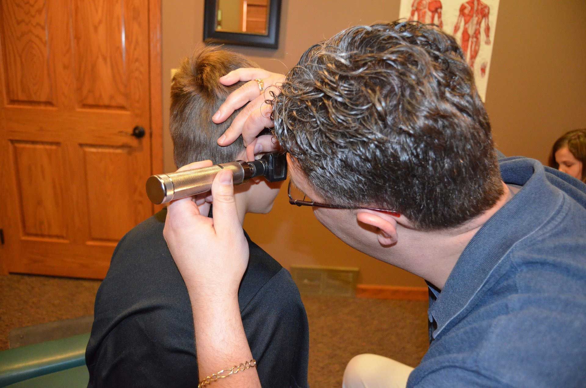 Doctor examining a young boy's ear with an otoscope in a doctor's office.