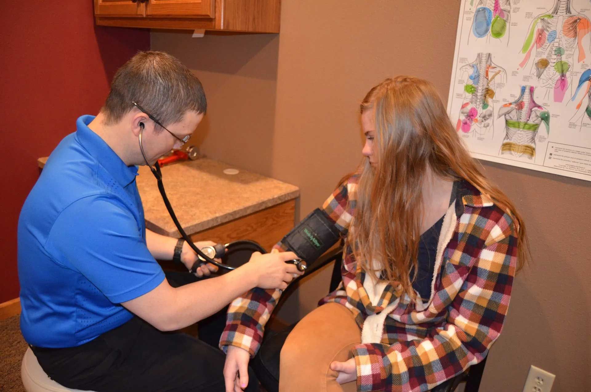 Doctor taking a young woman's blood pressure with a stethoscope in a doctor's office.