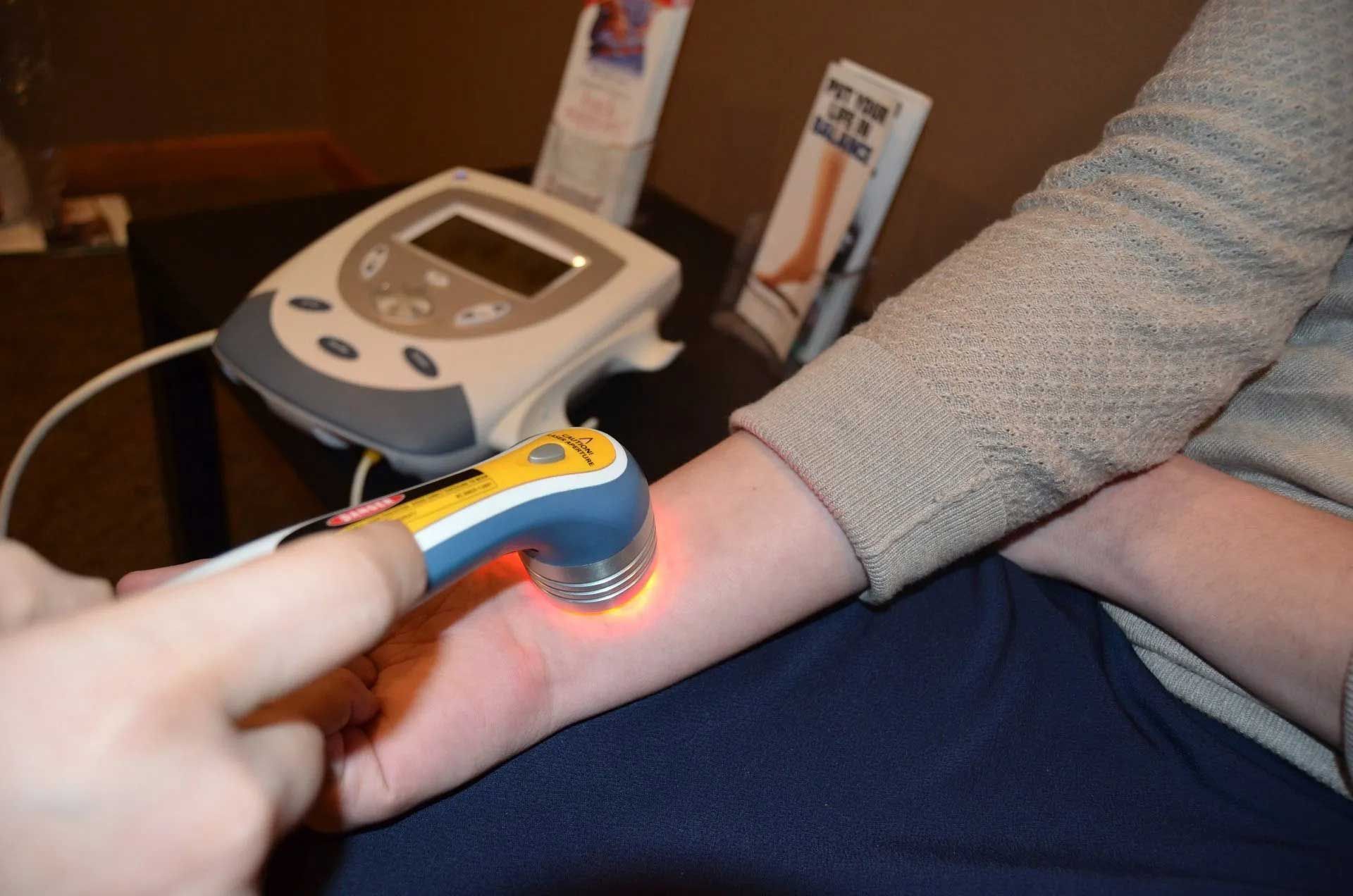 A person receiving laser therapy on their wrist; yellow and blue device with orange light.