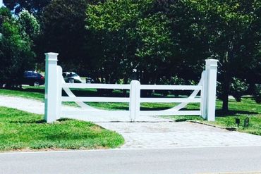 a white gate is open to a driveway with trees in the background
