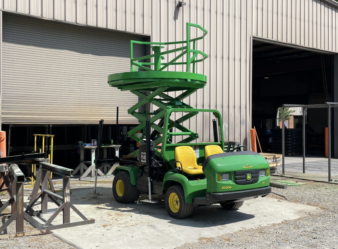 A green scissor lift is parked in front of a building.