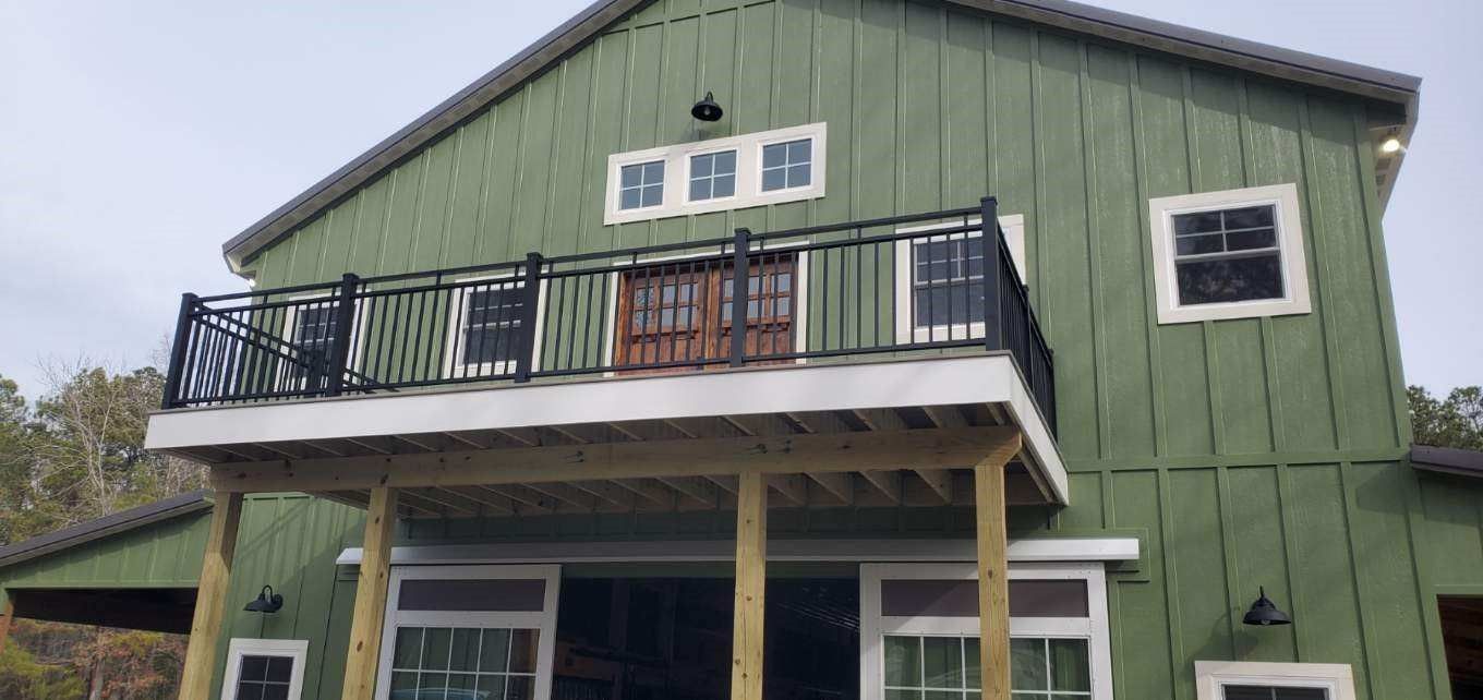 a green barn with a balcony and sliding glass doors