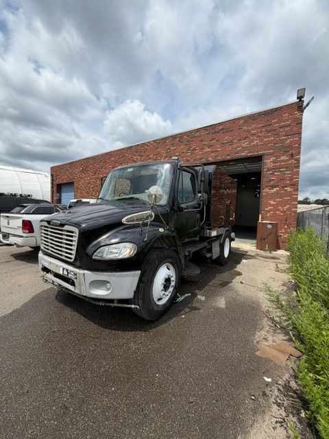 White semi-truck parked inside a warehouse garage, front view with lights on the cab.