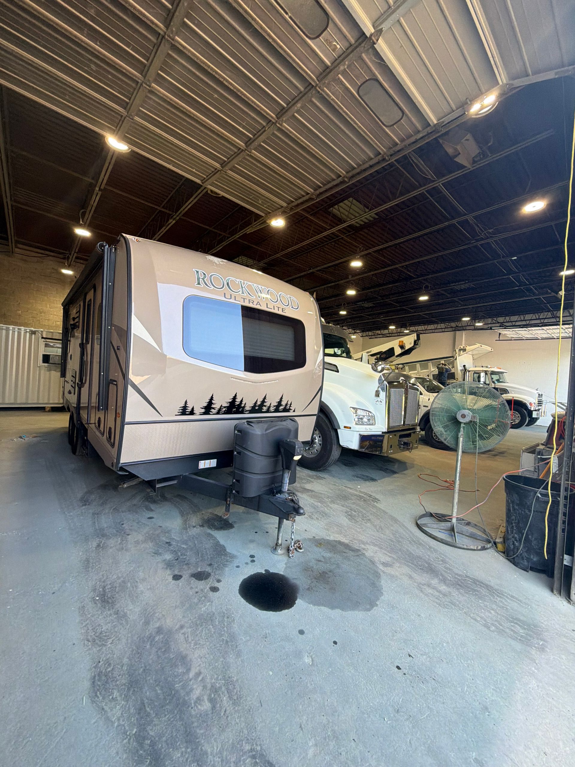 Camper trailer parked inside a warehouse with a white RV and equipment nearby.