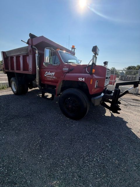Red dump truck parked on gravel under bright sunlight.