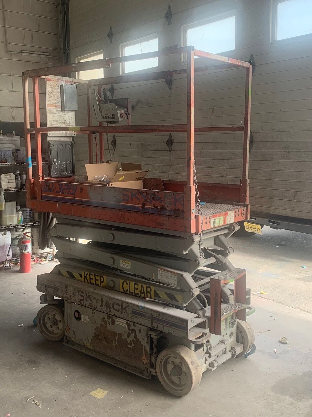 Scissor lift with an orange-railed work platform inside a warehouse, raised near a wall.