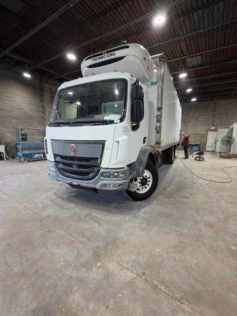 White refrigerated box truck parked inside a warehouse garage with concrete floor and overhead lights
