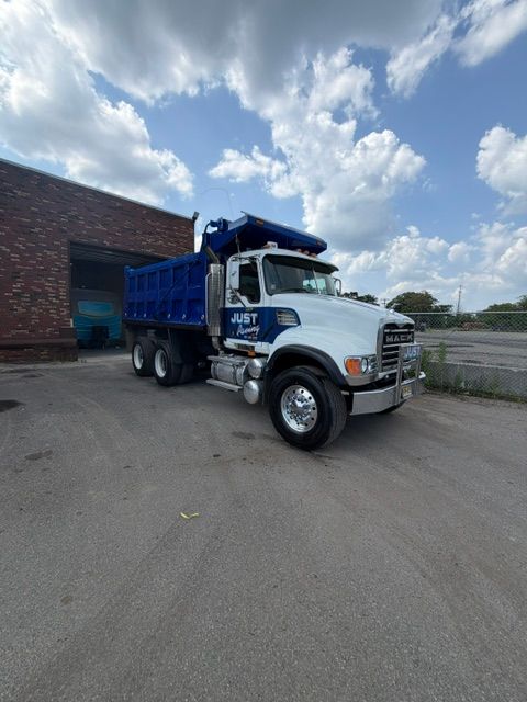 White dump truck parked beside a brick building under a partly cloudy sky