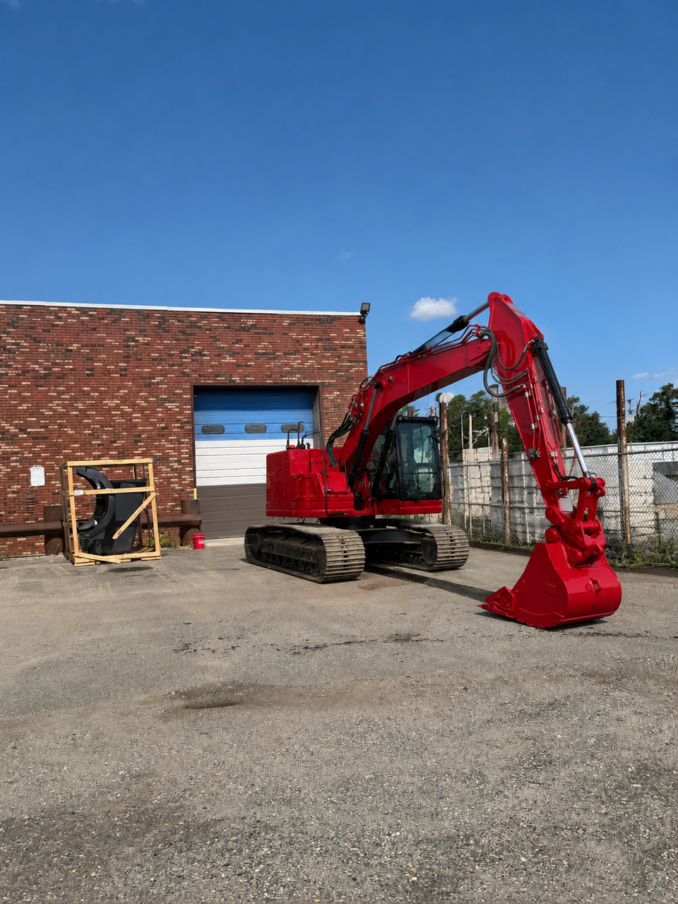 Red excavator parked beside a brick building under a clear blue sky.
