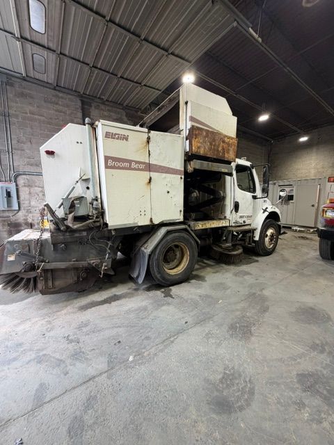 Red dump truck parked on gravel under bright sun, with front blade attachment visible.