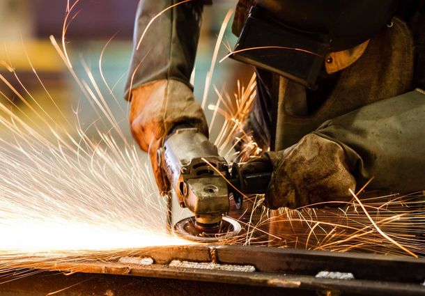 A man is grinding a piece of metal with sparks coming out of it.