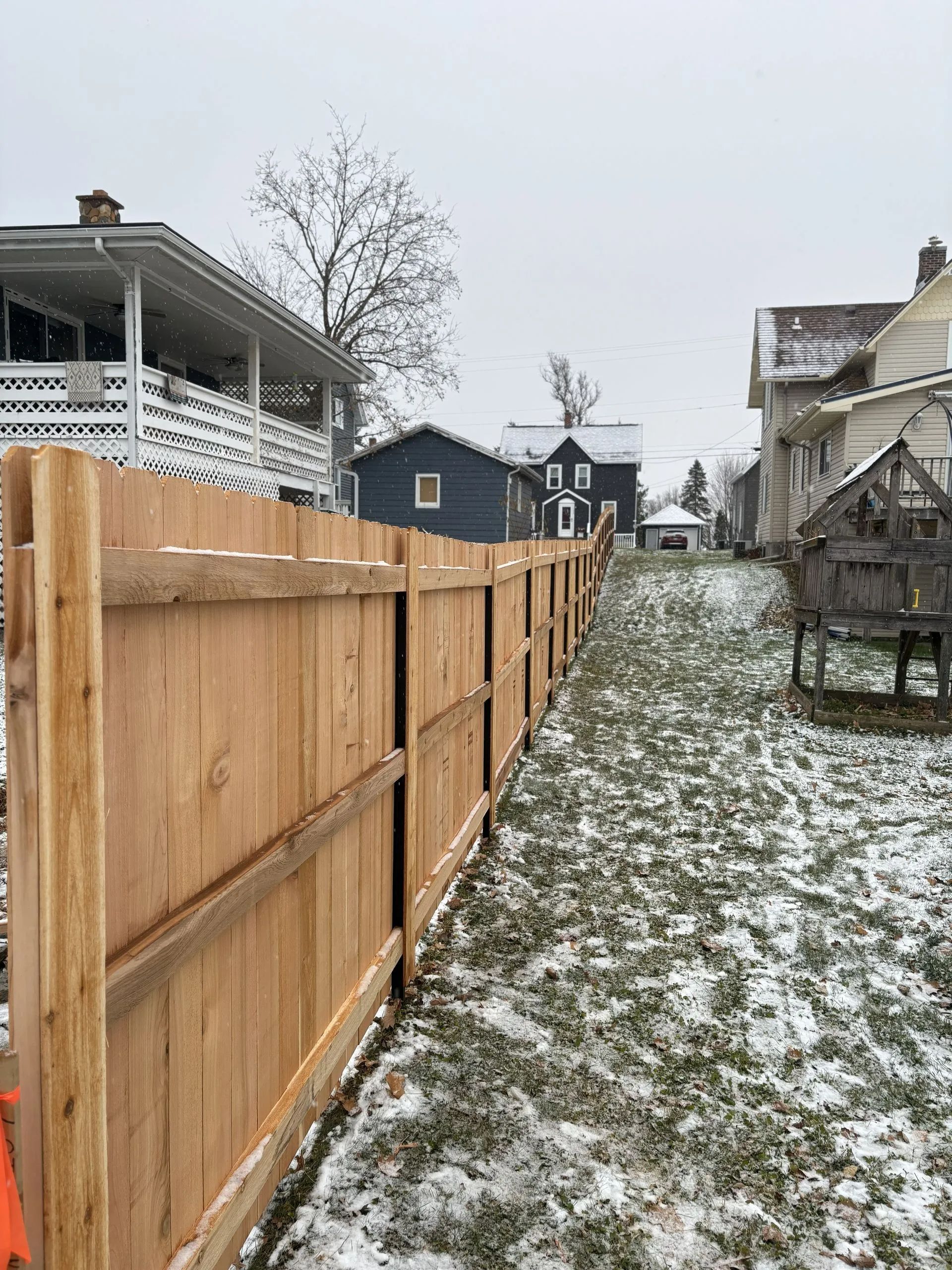 Wooden fence in a snow-covered yard, houses in the background.