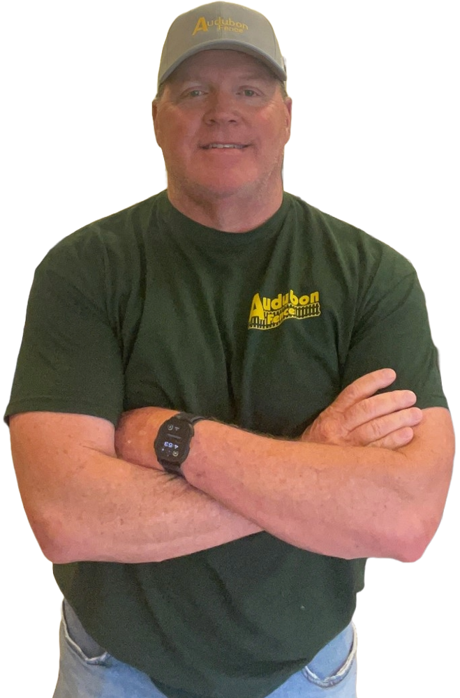 A man wearing a hat and a green sweater is standing with his arms crossed.