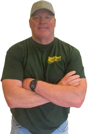 A man wearing a hat and a green sweater is standing with his arms crossed.