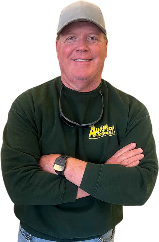 A man wearing a hat and a green sweater is standing with his arms crossed.