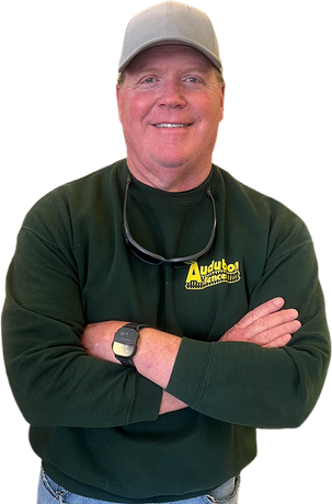A man wearing a hat and a green sweater is standing with his arms crossed.