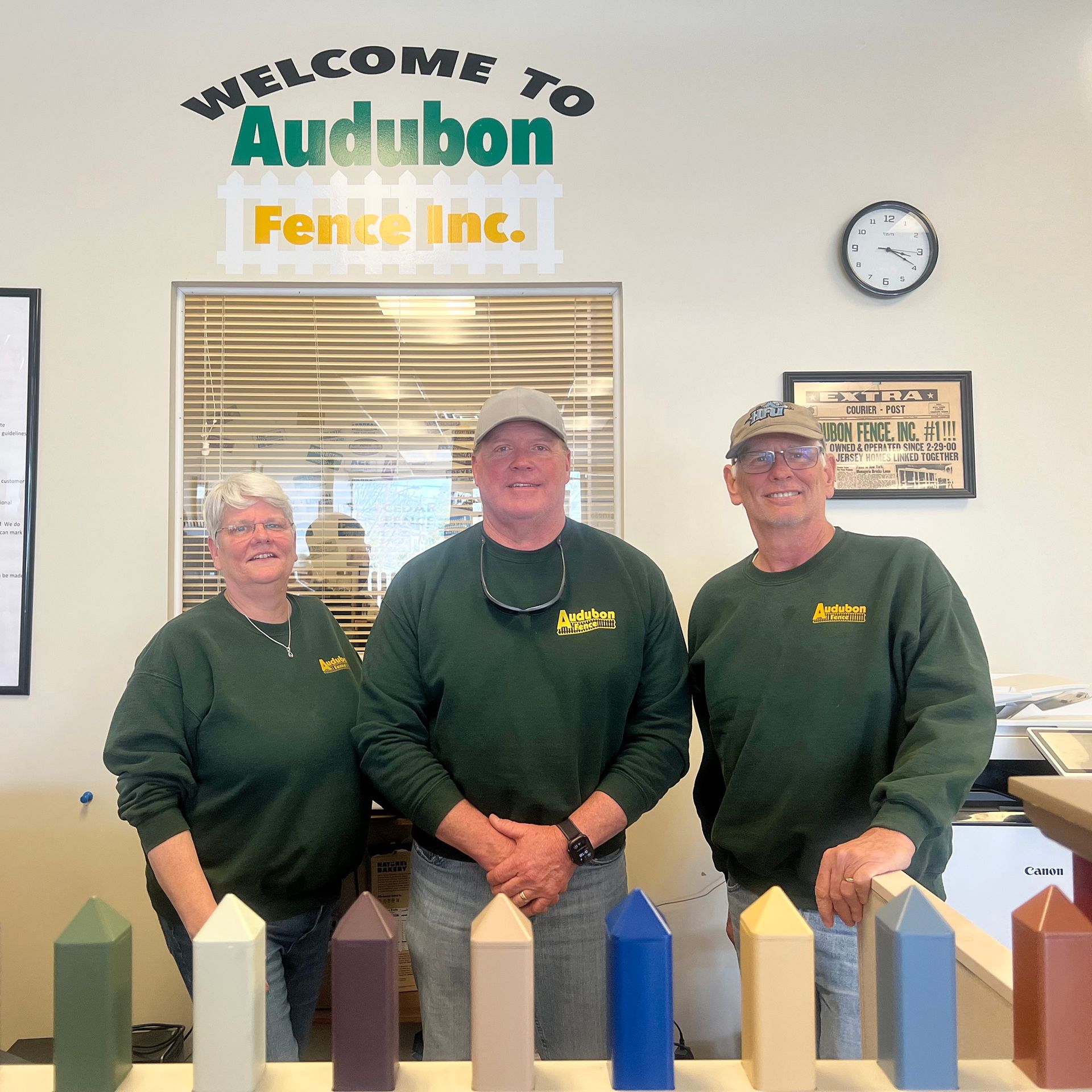 Three people standing in front of a sign that says welcome to audubon fence inc.