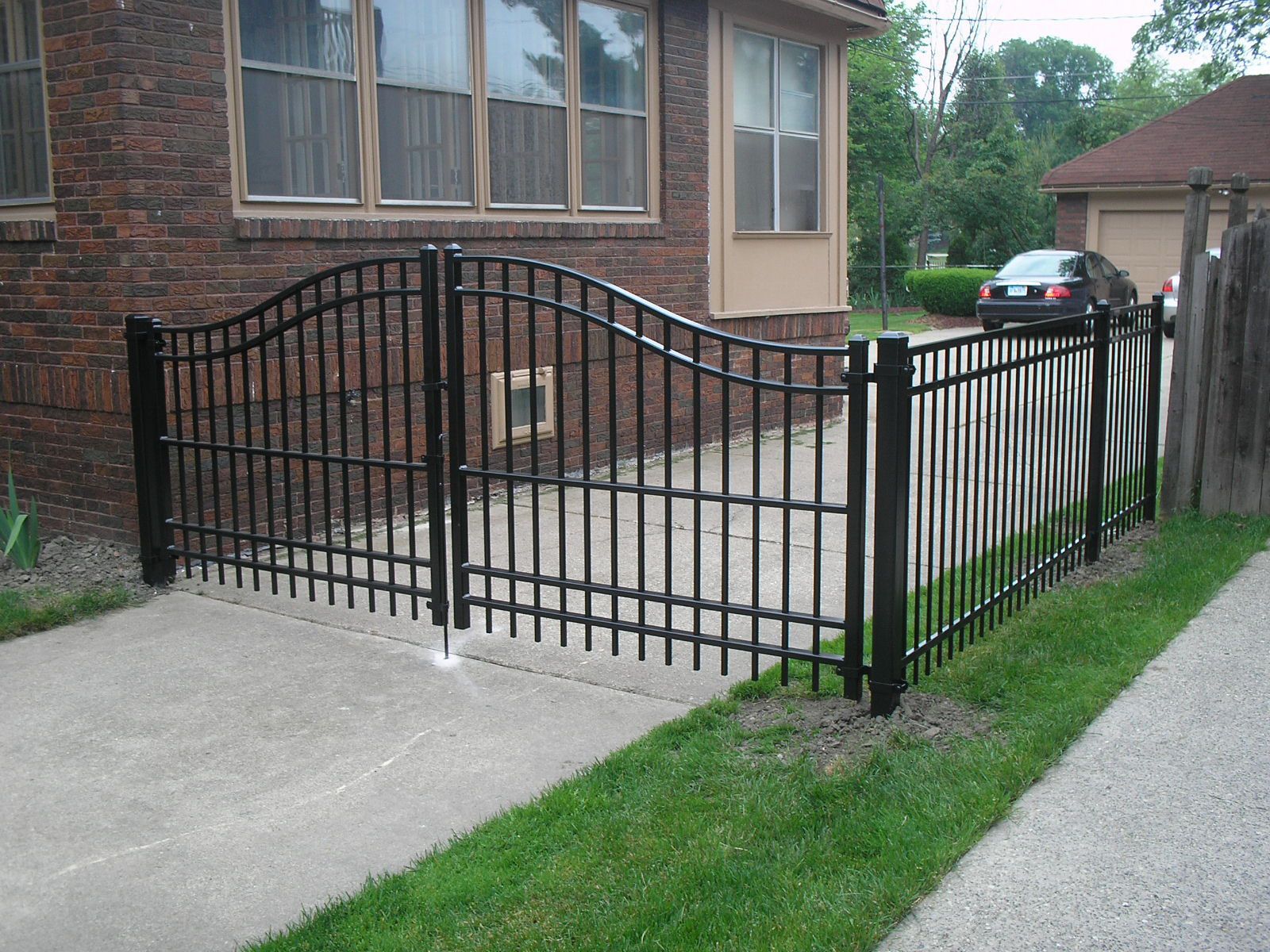 A black fence surrounds a driveway in front of a brick house