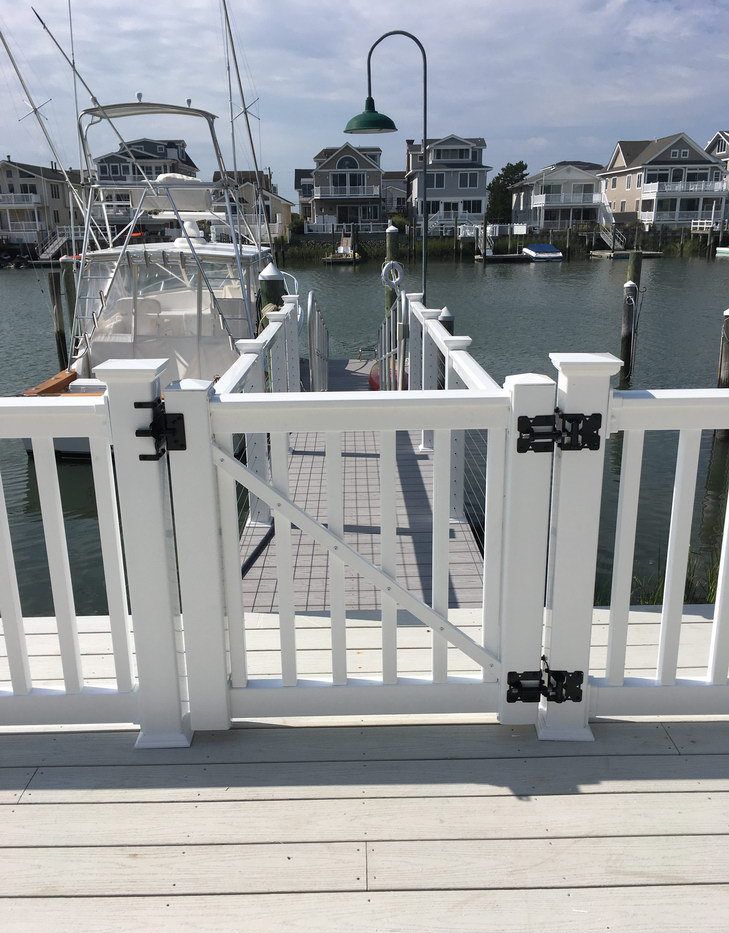 A white gate leading to a dock with boats in the background