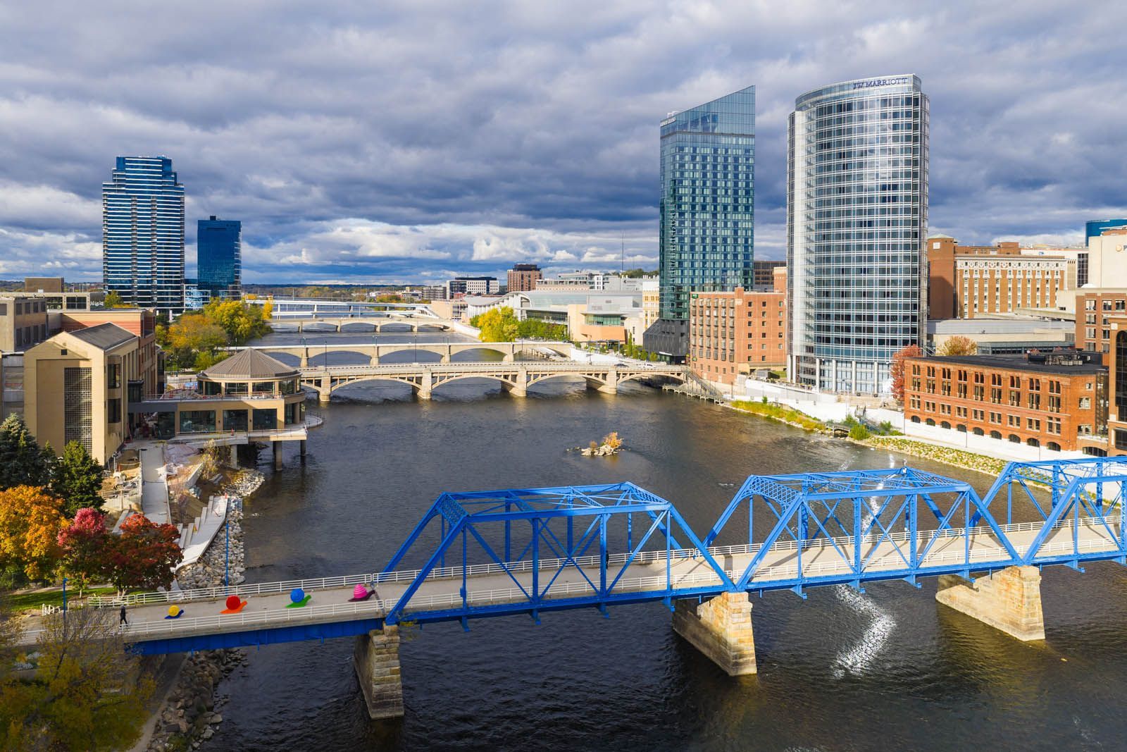 Blue bridge over river in downtown cityscape with tall buildings and cloudy sky