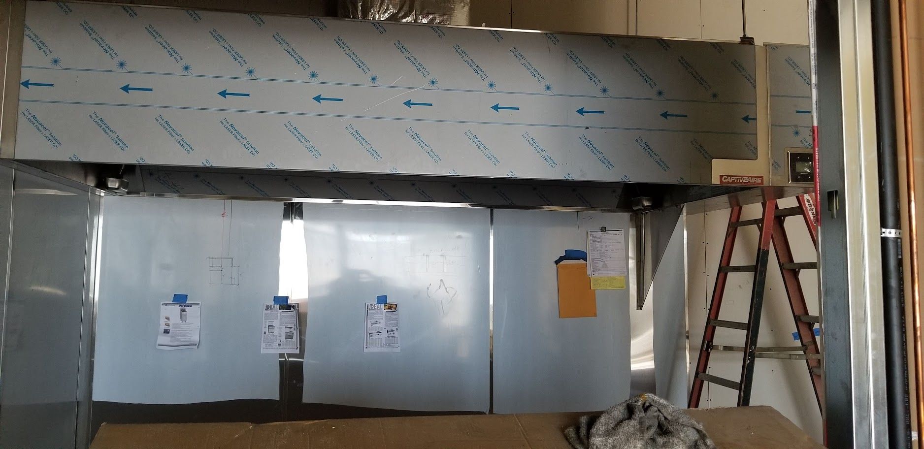 A ladder is sitting next to a stainless steel wall in a kitchen.