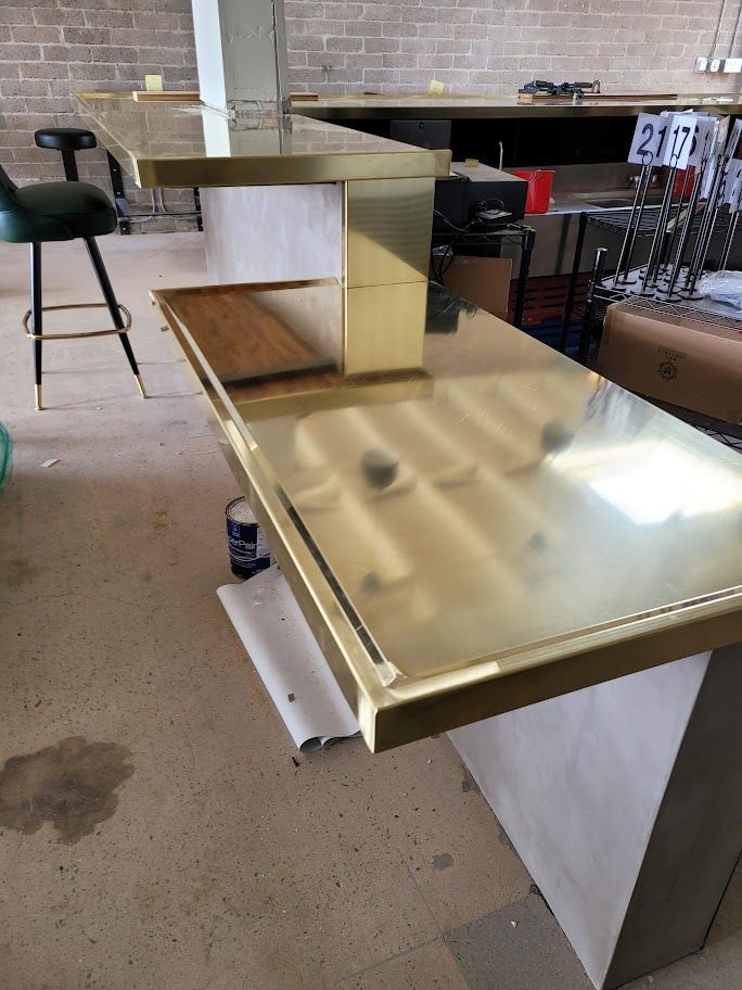 A table with a brass top is in a room with a brick wall.