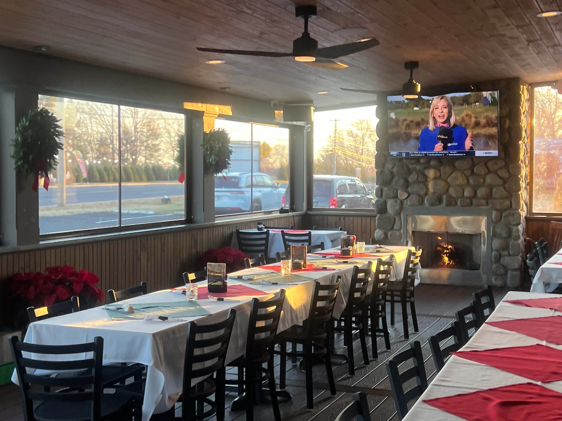 Dining room with long tables, red-and-white tablecloths, stone fireplace, and TV mounted above it