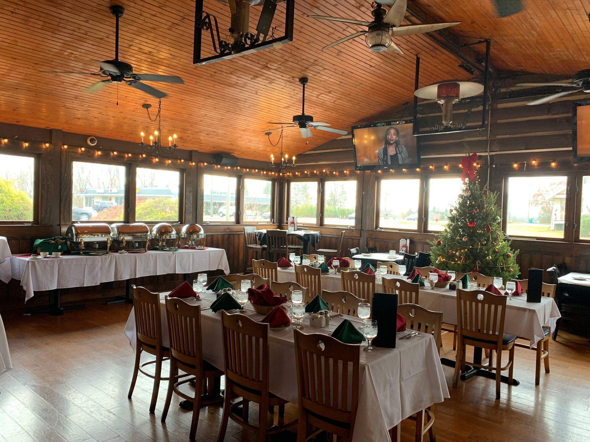 Empty restaurant dining room with white tablecloths, wooden chairs, and large windows.