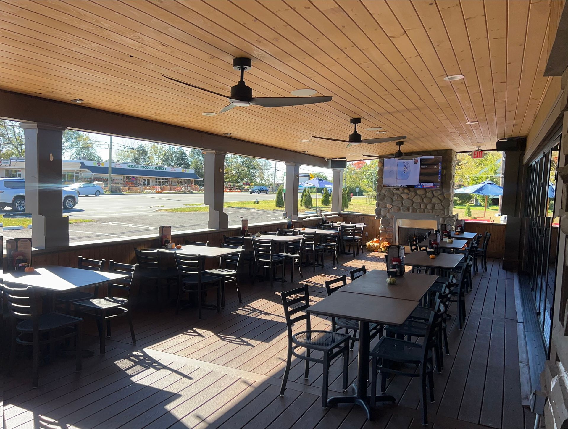Covered outdoor patio with tables and chairs, wooden ceiling, ceiling fans, and bright sunlight