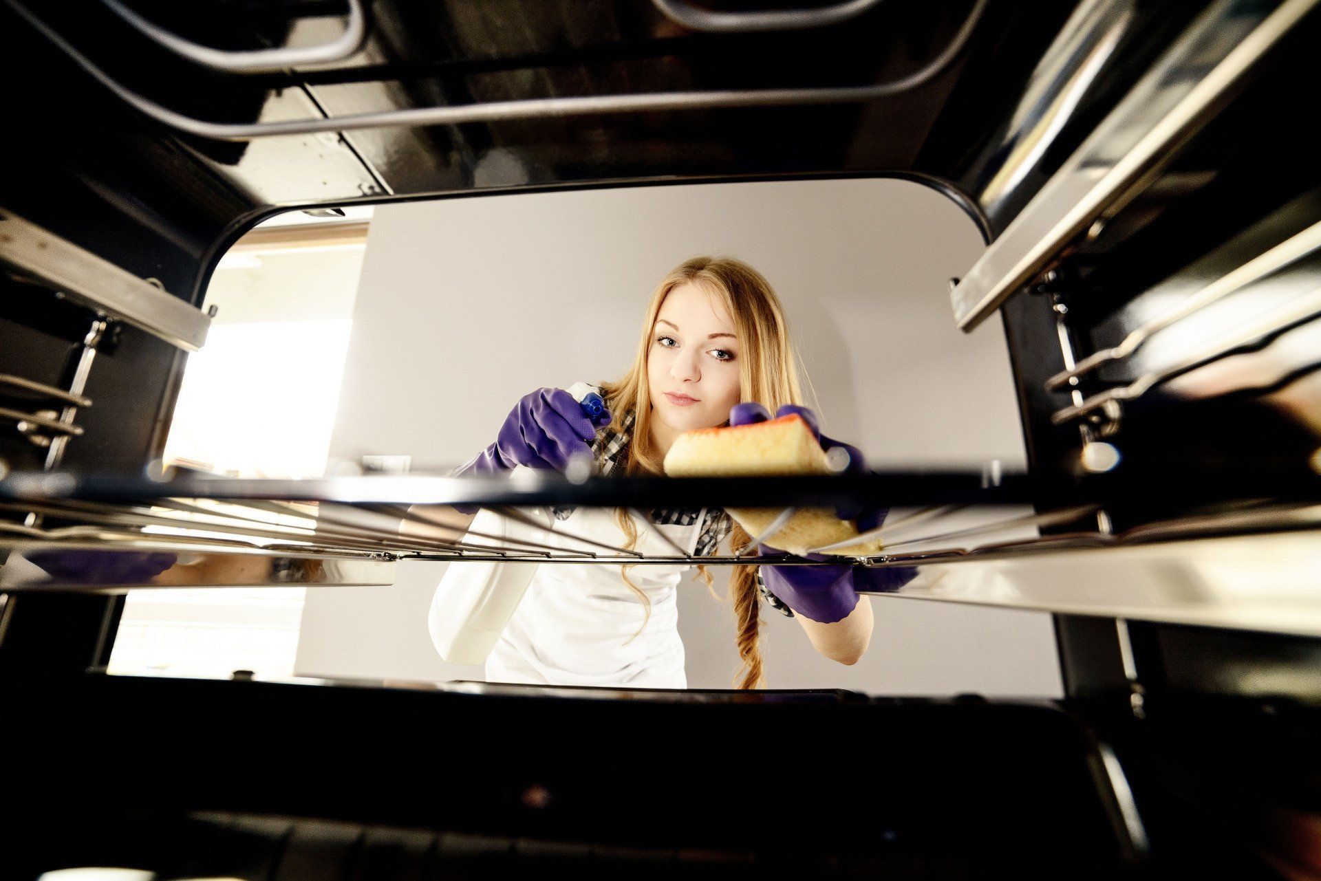 Woman cleaning inside of oven with sponge, wearing gloves, looking forward.