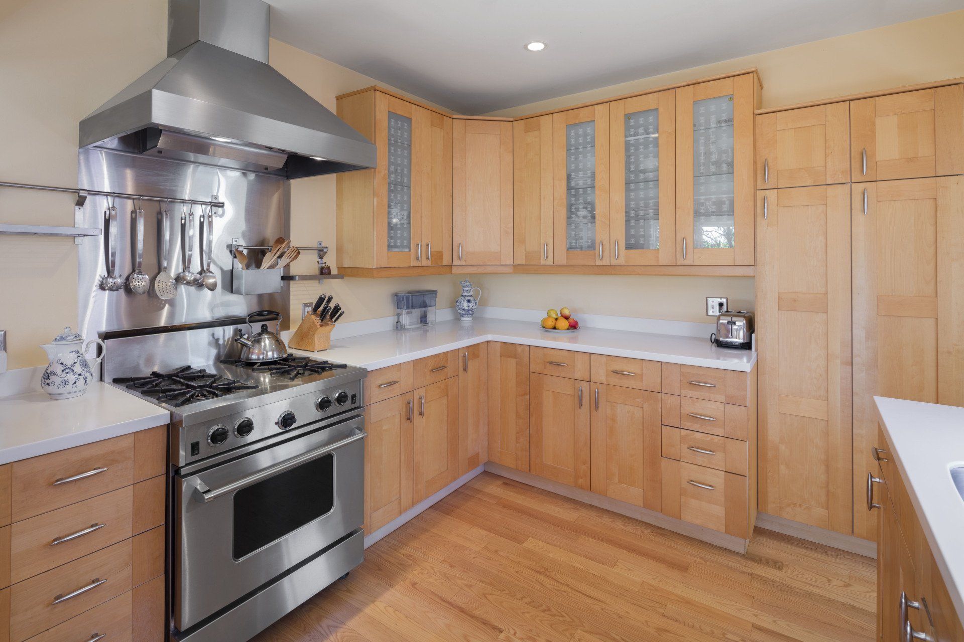 Modern kitchen with stainless steel appliances, light wood cabinets, and white countertops.