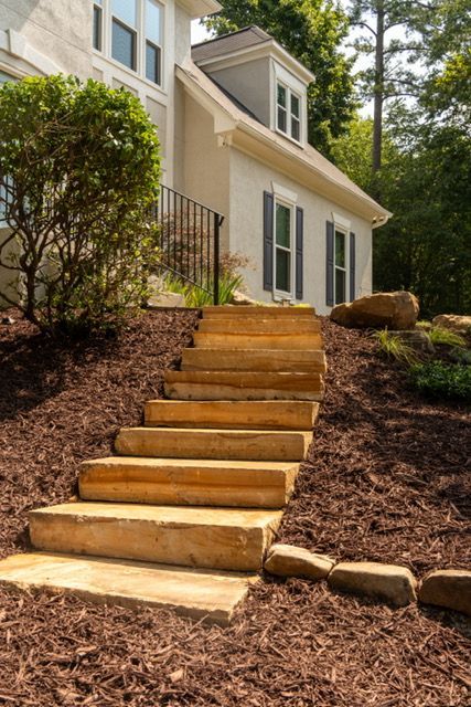 Stone steps leading up to a white house with shrubs and trees in a landscaped yard